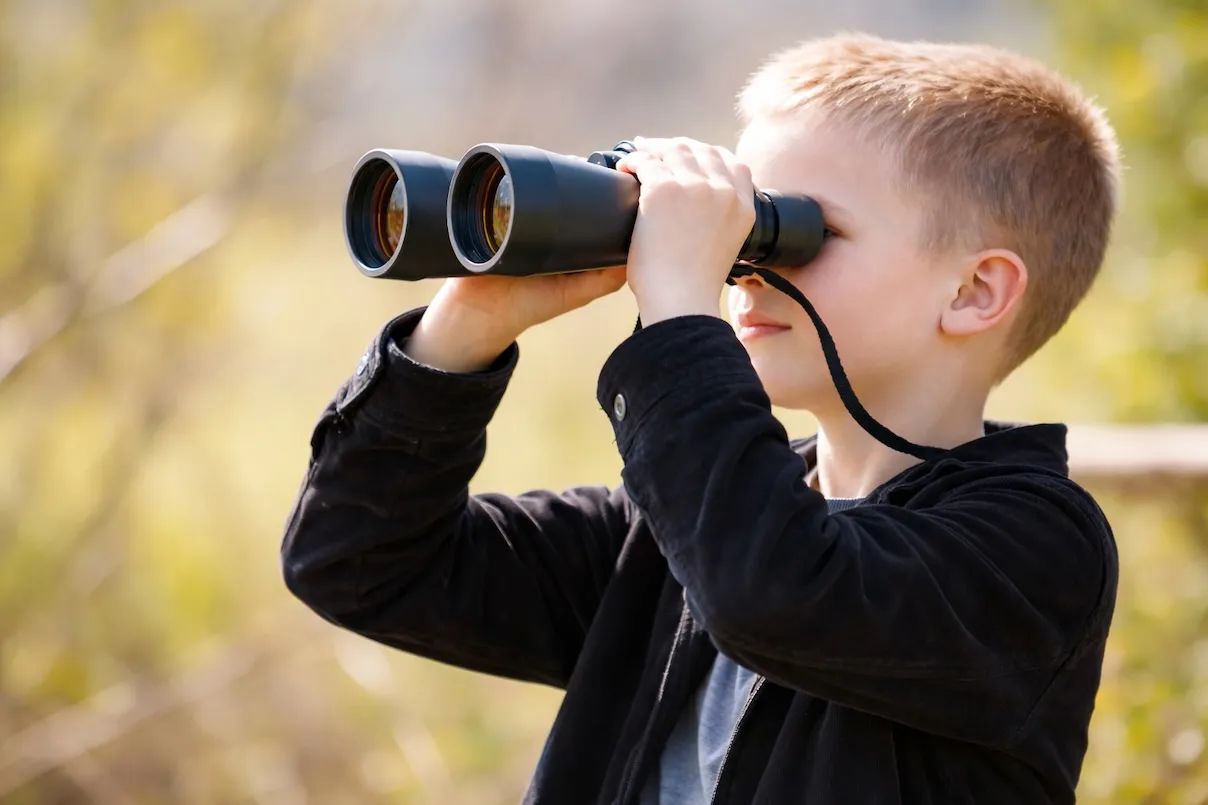 Bambino-che-guarda-attraverso-un-binocolo-all’aperto,-con-sfondo-naturale-sfocato.