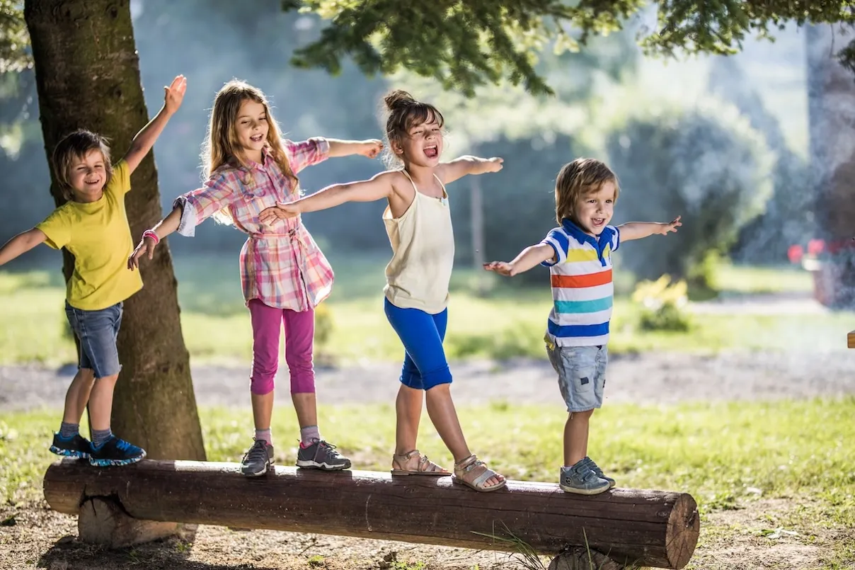 Gruppo di bambini che camminano sul tronco di un albero nella natura